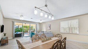 Un coin repas avec une table en bois, des chaises et un lustre. Une porte-fenêtre coulissante donne accès à un patio aménagé avec du mobilier d’extérieur.