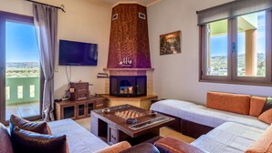 A spacious living room with a fireplace, a large TV, and a balcony with a scenic view.