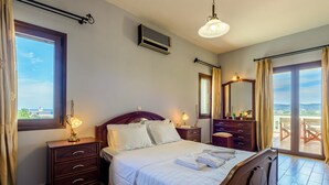 A well-lit bedroom with a bed, bedside tables, a dresser, and a large window offering a view.
