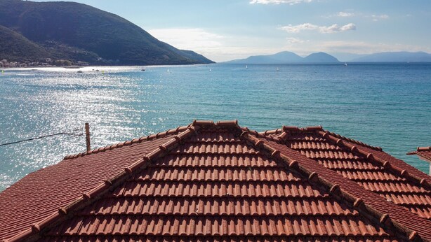 A coastal view with a tiled roof, calm sea, and distant mountains.