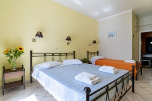 A double bed with a blue bedspread, two bedside tables, a nightstand, a vase with flowers, and two wall-mounted lamps.