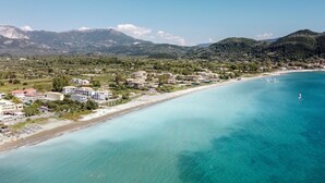 An aerial view of a coastal town with a beach, buildings, and mountains in the background.