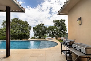 Uma piscina ao ar livre com borda curva, churrasqueira e pérgula.