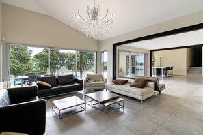 A spacious living room with a chandelier, two sofas, a coffee table, and large windows offering a view of the outdoors.