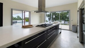 A modern kitchen with a large island, stainless steel appliances, and large sliding glass doors leading to an outdoor patio. - Villa 'Gecko' with Sea View, Wi-Fi and Air Conditioning (SARI SOLENZARA)