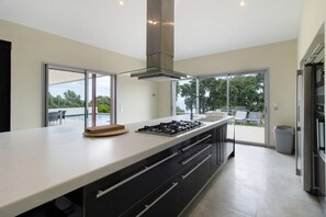 Cozinha moderna com uma ilha grande, eletrodomésticos de aço inoxidável e grandes portas de vidro deslizantes que dão para um pátio externo.
