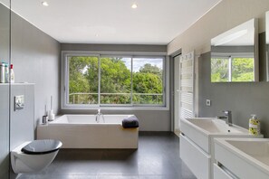 Um banheiro moderno com banheira, vaso sanitário e pia. Uma janela grande oferece vista para árvores.