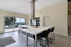 A modern kitchen with a central island, a dining area with chairs, and a view through glass doors.