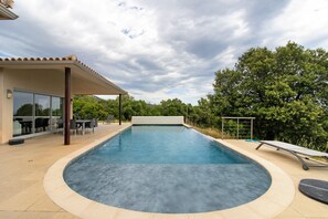 A swimming pool with a curved edge, surrounded by a covered patio area with outdoor furniture.