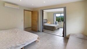 A bedroom with two beds, a sliding door leading to a balcony, and an air conditioning unit on the wall. - Villa 'Gecko' with Sea View, Wi-Fi and Air Conditioning (SARI SOLENZARA)
