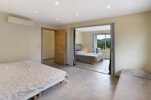 A bedroom with two beds, a sliding door leading to a balcony, and an air conditioning unit on the wall.
