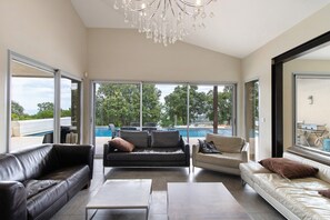 Ampla sala de estar com vista para a piscina, um candelabro e design de interiores moderno.