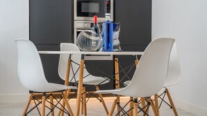 Una cocina moderna con una mesa blanca, dos sillas blancas, una botella azul y un microondas.