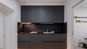 Una cocina moderna con muebles oscuros, un lavamanos de acero inoxidable y un horno empotrado.