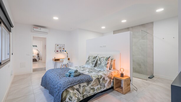 Un dormitorio moderno con cama, mesita de noche y zona de ducha.