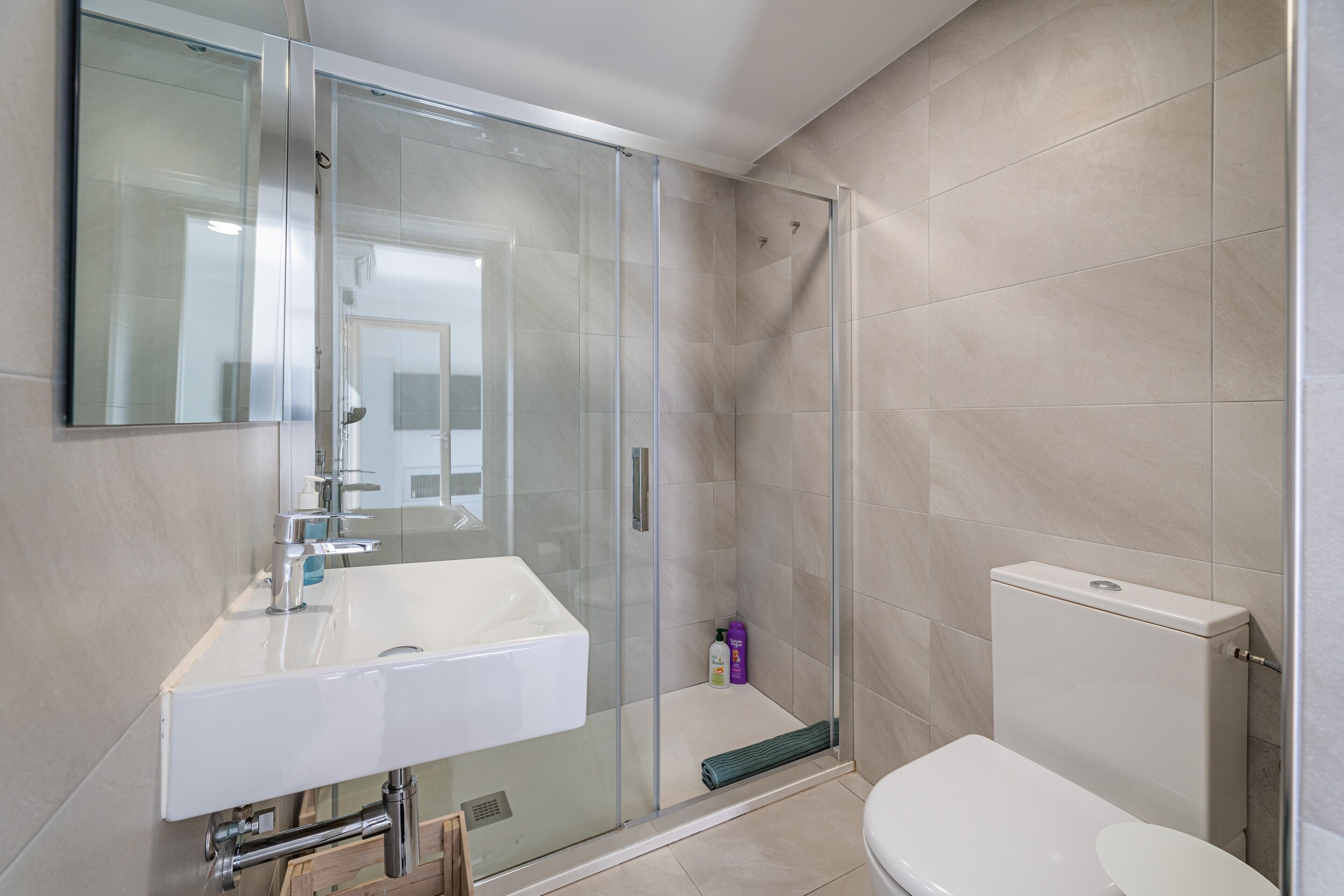 Un baño moderno con ducha de vidrio, lavamanos blanco y retrete.