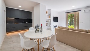 Una cocina moderna con armarios oscuros, una mesa de comedor blanca con sillas, un sofá y un televisor en la pared.