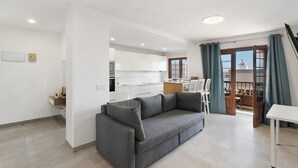 Una sala de estar moderna con un sofá gris, un comedor con sillas y una cocina al fondo.