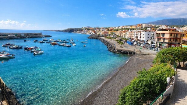 Un pueblo costero con aguas azul turquesa, barcos y edificios a lo largo de la costa.