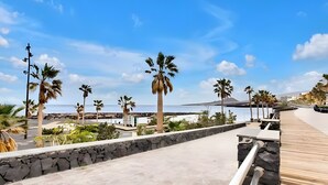 Un paseo marítimo con palmeras, un muro de piedra y una terraza de madera.