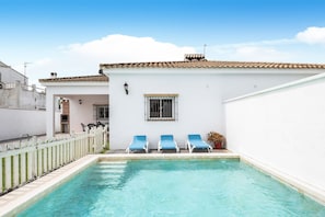 A swimming pool with three lounge chairs, a white building with a tiled roof, and a white fence. - Chalet Casa Playamar near the beach with garden, pool and Wi-Fi (Vejer de la Frontera)