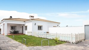Una casa blanca con techo de tejas, piscina cercada y patio con mobiliario exterior.