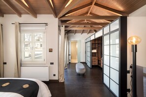 Habitación de hotel con techo de madera, un ventanal con persianas, un banco y una lámpara.