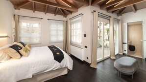 A bedroom with a large bed, a small stool, and a sliding glass door leading to a balcony. - Located in the Heart of Heraklion, combining Elegance & Modern Luxury.  (Iraklio)
