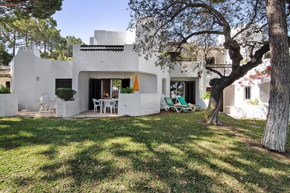 A white building with a patio area, outdoor seating, and a tree.