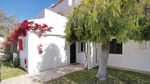 A white building with a paved entrance, a tree with green foliage, and a red fire extinguisher mounted on the wall. - Balaia Apartment near the Beach with Shared Pools (Albufeira)