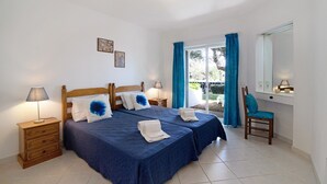 A double bed with two pillows, a nightstand with a lamp, a chair, and a window with curtains. - Balaia Apartment near the Beach with Shared Pools (Albufeira)