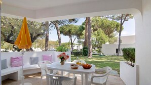 A patio with a white table, chairs, a yellow umbrella, and a white bench with cushions. - Balaia Apartment near the Beach with Shared Pools (Albufeira)