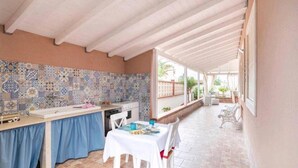 Un área de comedor al aire libre techada, con un salpicadero de azulejos, una mesa dispuesta con platos y sillas.