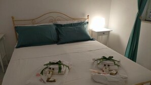 Una cama con estructura metálica, dos almohadas, una mesita de noche y un buró.