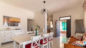 Un área de comedor con una mesa y sillas, un sofá, un cuadro y una cocina al fondo.
