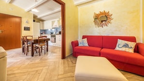 Una sala de estar con un sofá rojo, una mesa de comedor de madera con sillas y una cocina al fondo.