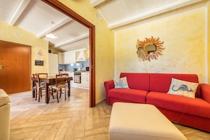 A living room with a red sofa, a wooden dining table with chairs, and a kitchen in the background.