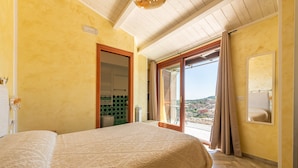 Un dormitorio con cama, puerta corrediza de vidrio a un balcón y vista de la ciudad.
