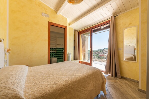 A bedroom with a bed, a sliding glass door to a balcony, and a view of the city.