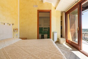 A bedroom with a large bed, a sliding glass door to a balcony, and a view of the city.