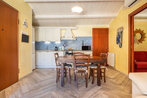 A dining area with a wooden table and chairs, a kitchen in the background, and a red sofa in the foreground.