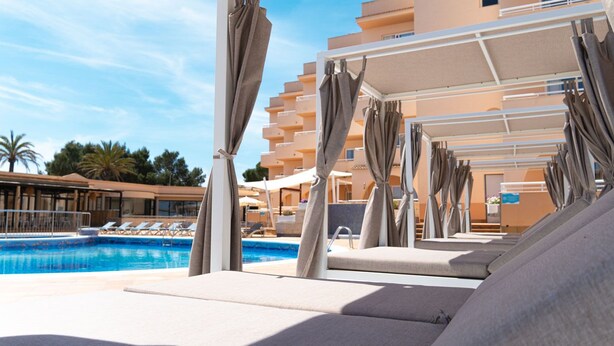 A poolside area with lounge chairs and umbrellas, a clear blue pool, and a building with balconies in the background. - Rosamar Ibiza Hotel (Sant Josep de sa Talaia)
