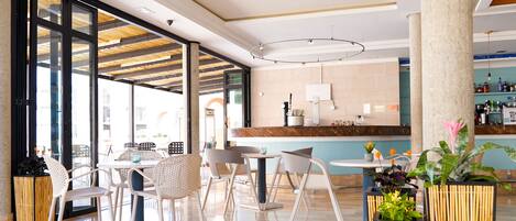 A modern indoor space with a bar area, seating arrangements, and large windows allowing natural light.