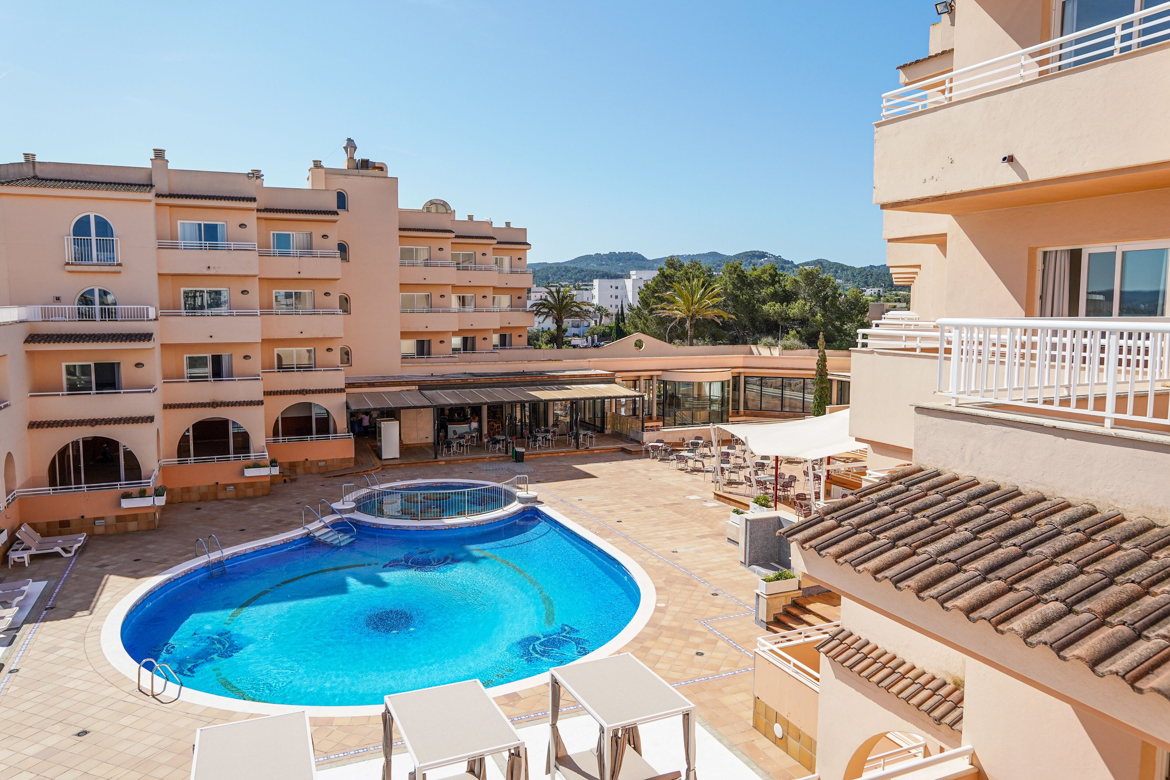 Una piscina envoltada de mobiliari exterior i un edifici amb balcons.