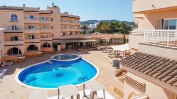 Una piscina envoltada de mobiliari exterior i un edifici amb balcons.