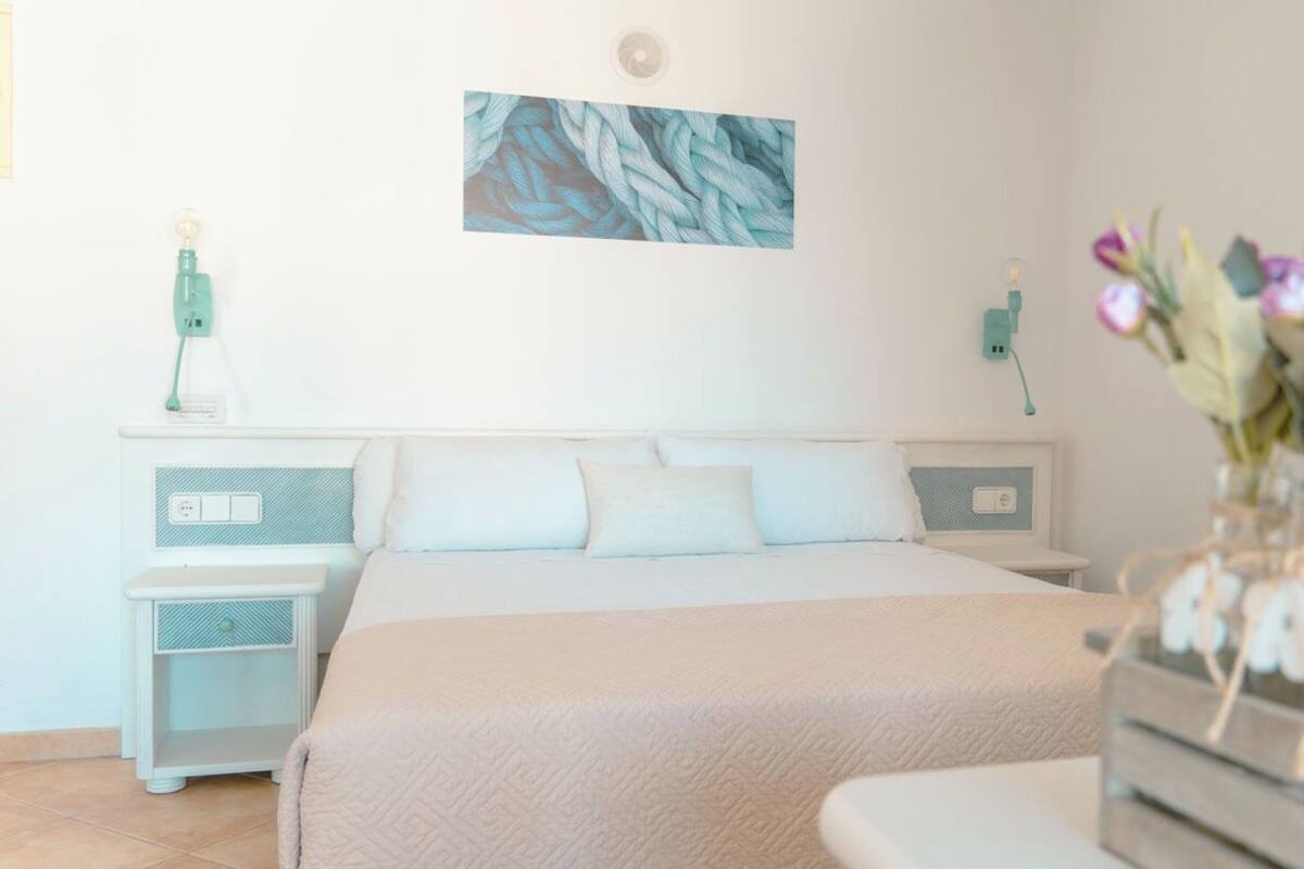 Une chambre à coucher avec un lit, des tables de chevet, une lampe fixée au mur et un vase avec des fleurs.