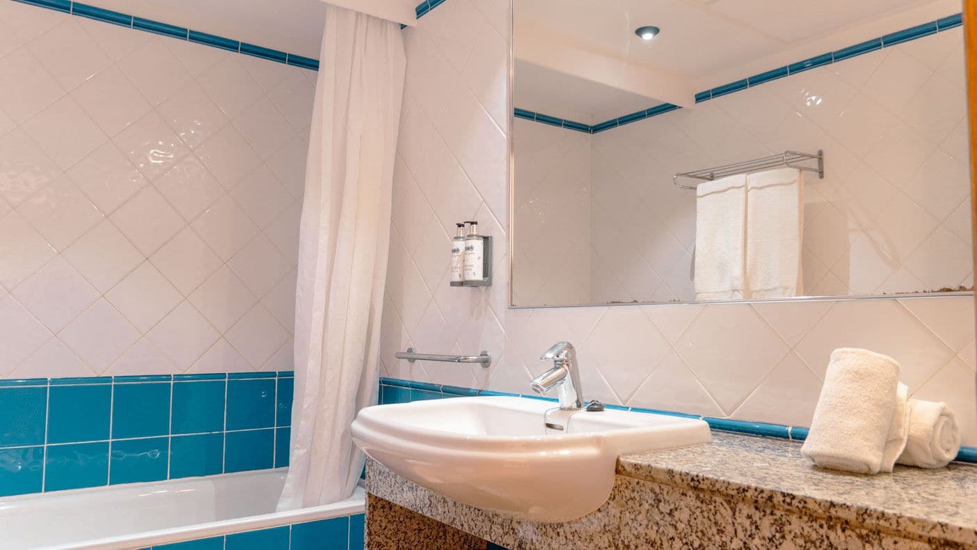A bathroom with a white sink, blue-tiled walls, a shower curtain, and a towel on the counter.