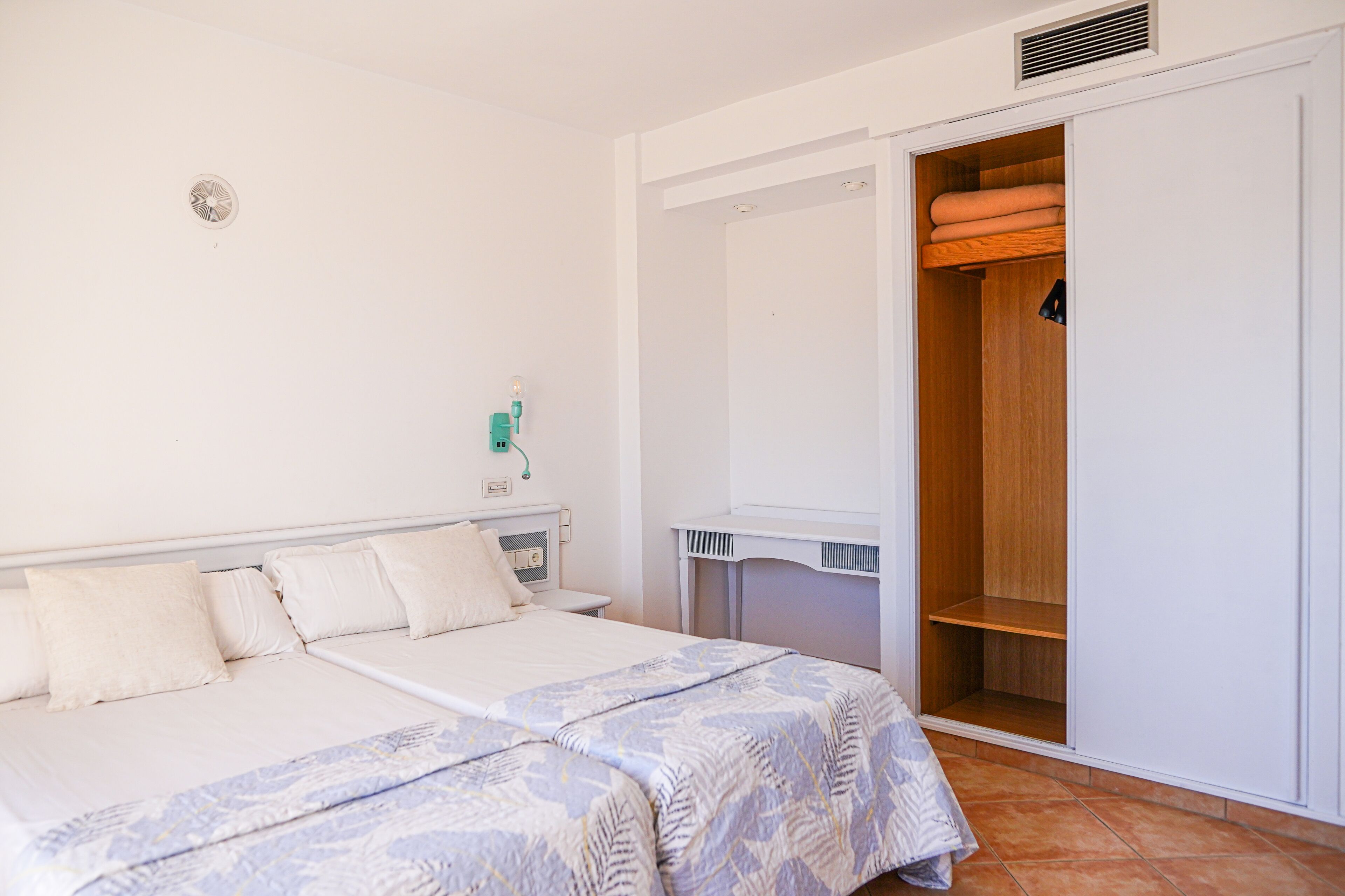 A bedroom with a bed, bedside tables, a wardrobe, and a wall-mounted light fixture.