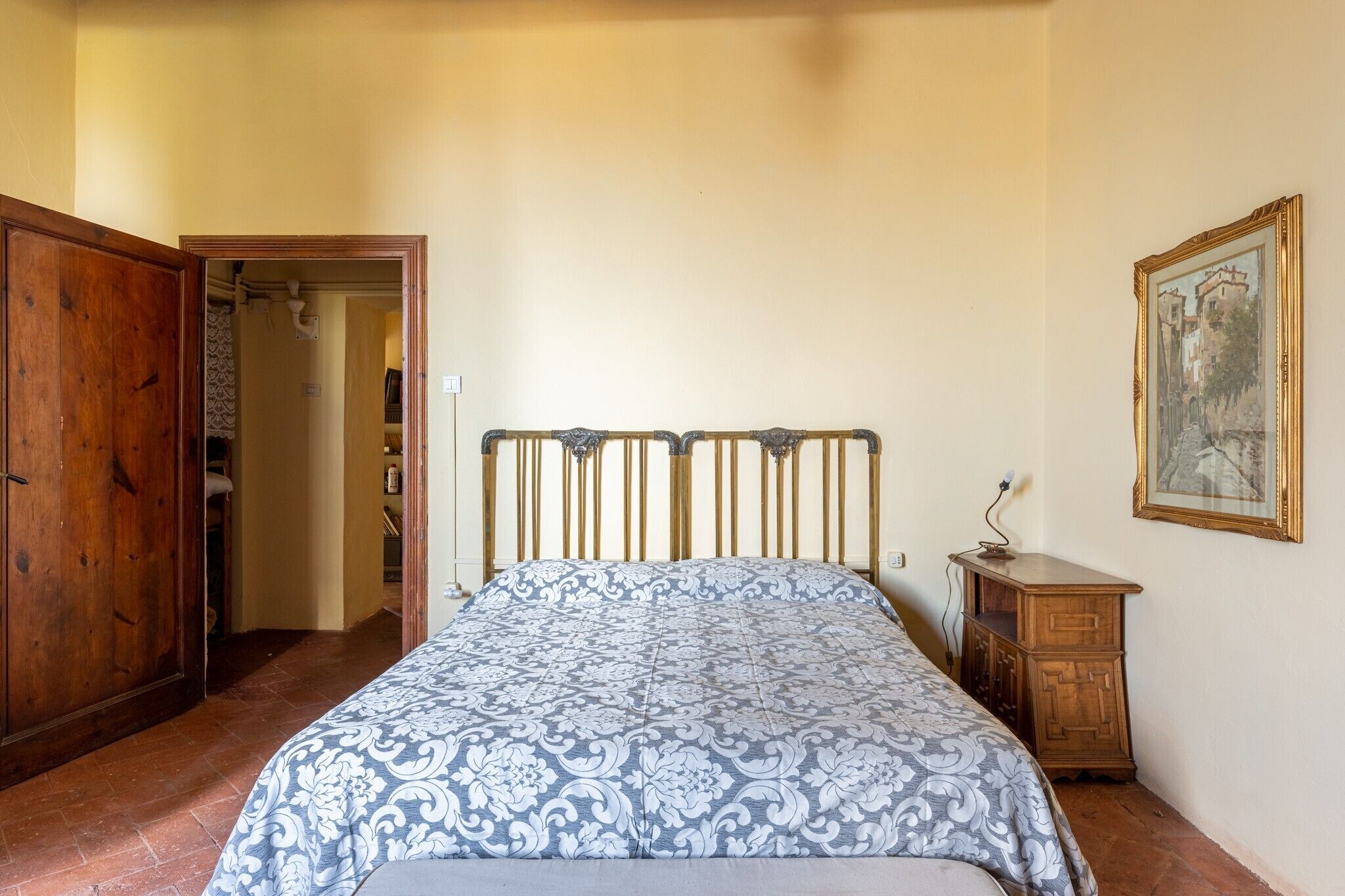 Een slaapkamer met een bed, een houten garderobe, een klein nachtkastje en een schilderij aan de muur.