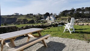 A picnic table and chairs in a grassy area with a view of houses and a statue in the background.